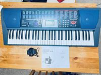 Top view of Casio CTK-501 keyboard showing 61 keys, control panel with buttons and screen, built-in speakers, placed on a wooden table.