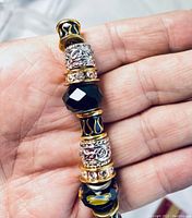 Close-up of the beaded necklace segment showing black faceted glass beads, floral-patterned black beads, silver-tone filigree barrel spacers, and gold-tone rhinestone rings.