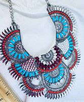 Close-up photo showing fan-shaped segments of the necklace with red, turquoise, and clear stones set in silver-tone metal.