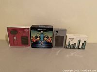 Overview of four sealed boxed items: Jogi hot stone massage kit, Jean Paul Gaultier Le Male set, Rocawear 9 IX, Sex in the City Kiss Men.