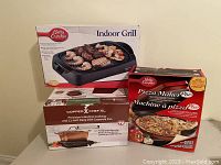 Photo of all three boxed kitchen items grouped together showing their packaging: Betty Crocker Indoor Grill, Betty Crocker Pizza Maker Plus, Copper Chef Precision Induction Cooker and Deep Dish Casserole Pan