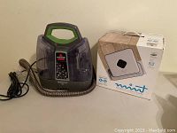 Bissell SpotClean PET spot cleaner and box of Mint automatic floor cleaner on table.