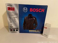 Box of Bosch heated jacket with Diesel cologne beside it, showing front product packaging and branding.
