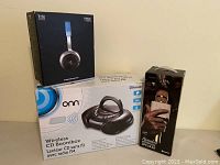 Boxed Ferrara Design T250 headphones, Onn wireless CD boombox, and iWave karaoke microphone in their original packaging, displayed on a table.