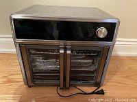 Front view of the Kalorik Maxx Air Fryer Oven Grill showing metallic finish and dual glass doors with handles and control knob.