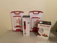 Photo showing two red and white cutting boards, KitchenAid hand blender box, and KitchenAid stand mixer attachment box.
