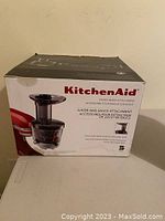 Photo of boxed KitchenAid juicer and sauce attachment showing the brand and main product image on the front of the box.