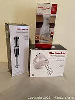 Three KitchenAid appliances in original boxes showing mixer, hand blender, and chopper.