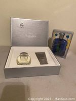 Open box of Estée Lauder Pleasures for Men gift set with clear glass bottle and grey after shave balm tube, next to Ralph Lauren Big Pony #1 gift set packaging