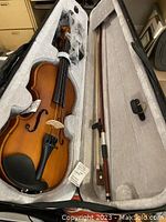 Violin, bow, and accessories organized inside the soft carrying case, showing the plush light grey interior.