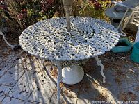 Full view of round white cast aluminum metal table placed outdoors, showing ornate scrollwork top and curved legs.