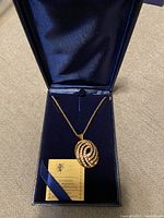 Gold-tone necklace displayed in blue velvet box with satin lining, showing full necklace and pendant.