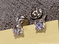 Front view of both earrings showing round diamonds and push-back closures on fabric background