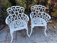 Two white metal chairs on stone patio, front view