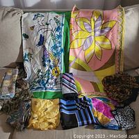 Eight scarves displayed on a couch, two laid flat and six folded below