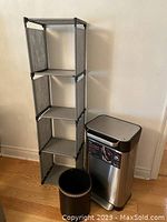 Gray fabric 4-tier storage shelf and Titan trash compactor placed on hardwood floor against wall.