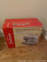 Box front showing Sunbeam logo and image of the sewing machine model SB700 with text listing features like 70 built-in stitch patterns and simple dial stitch selector.