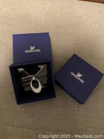 Swarovski pendant necklace displayed inside a dark blue Swarovski branded box with lid beside it.
