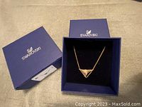 Swarovski box with the necklace inside, showing the blue branded packaging and the pendant necklace inside with gold-tone chain and triangular pendant.