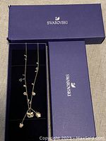 Gold tone Swarovski necklace with multiple charms inside its branded box