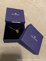 Blue Swarovski box with necklace displayed on black velvet interior, lid partially open showing logo.