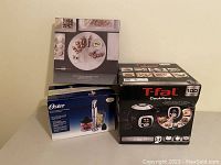 Photo showing the boxed T-fal Cook4me multicooker alongside the boxed Oster immersion blender and a cookbook.