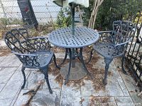 Overall view of round lattice-top table with umbrella pole installed and two matching chairs on stone patio