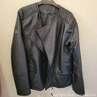 Front view of black leather jacket showing quilted design on shoulders and cuffs, asymmetrical zipper, and zippered pockets.