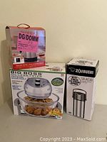 Photo of three boxed kitchen appliances: Paderno electric kettle on left, Big Boss oil-less fryer in center, and Zojirushi stainless steel beverage dispenser on right.