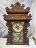 Full front view of antique gingerbread clock showing carved walnut case and etched glass door revealing pendulum and clock face.