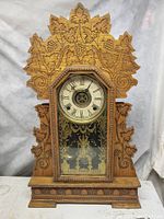 Front view of the oak gingerbread mantle clock showing detailed carved leaf and grapevine design on wood and the clock face behind the glass door.