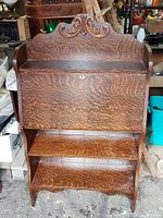 Front view of 1920s maple drop front secretary desk showing carved top and two shelves