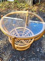 Photo of the round bamboo coffee table showing the glass top and bamboo base outdoors on gravel with autumn leaves.