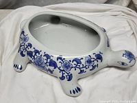 Full view of white ceramic turtle vessel with blue floral decorations and shaped feet and head.