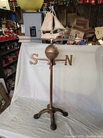 Full view of weathervane standing on tripod base against backdrop