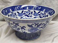 Large blue and white ceramic footed fruit bowl with floral designs on white background, shown from front angle
