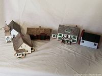 Front view of the five Hallmark miniature buildings arranged in a row on a neutral fabric background.