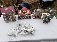 All 5 ceramic Christmas village buildings with light sockets and cords spread on white cloth