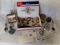 Full lot displayed on white cloth, showing jewellery and various small collectibles including postcards, spoons, and cases.