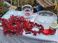 Christmas decorative items including red berry wreaths, garlands, ceramic Christmas boot, crystal glass bowls, and boxed coasters on a table.