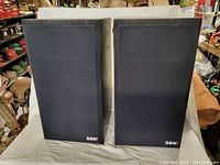 Front view of both speakers with black fabric grilles on, B&W logos visible on bottom right corner of each grille.