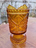 Front angled view of vintage amber pressed glass celery holder showing detailed geometric patterns and scalloped rim.