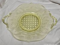 Top-down view of a translucent yellow Depression glass platter showing detailed floral embossing and geometric center pattern with handles on each side.