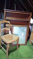 Full view of the wood bookshelf, chair with caned seat, and wood frame mirror on green carpeted floor, inside attic.