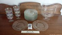 Photo of large clear glass trifle bowl, stack of 18 clear glass plates, and two stemware glasses with iridescence