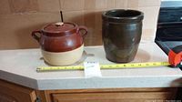 Two ceramic crocks on kitchen counter, one with lid and handles and one open vessel.