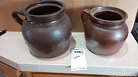 Two ceramic crocks side by side showing different sizes and shapes each with a single handle under the rim