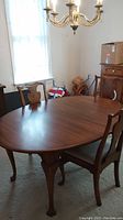 Wooden oval-shaped dining table with 4 visible chairs, window light in background.