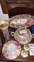 Full view of porcelain gold and rose set displayed together showing soup tureen, tray, vase, salt and pepper shakers, and floral plate.