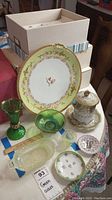 Photo showing all collected green glass and porcelain items on a table including plates, bowls, goblet/vase, and lidded dish.